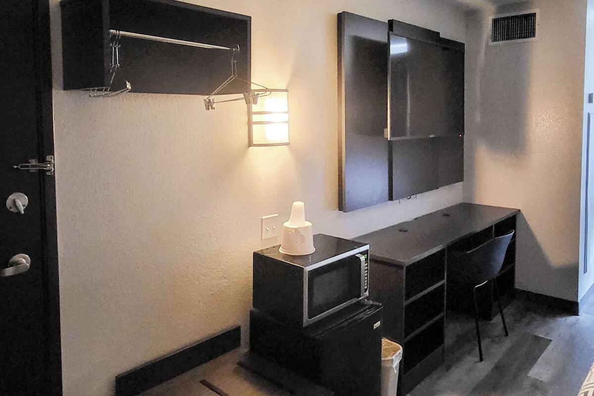 A compact hotel room with a kitchenette, a large mirror, a desk, and a chair.