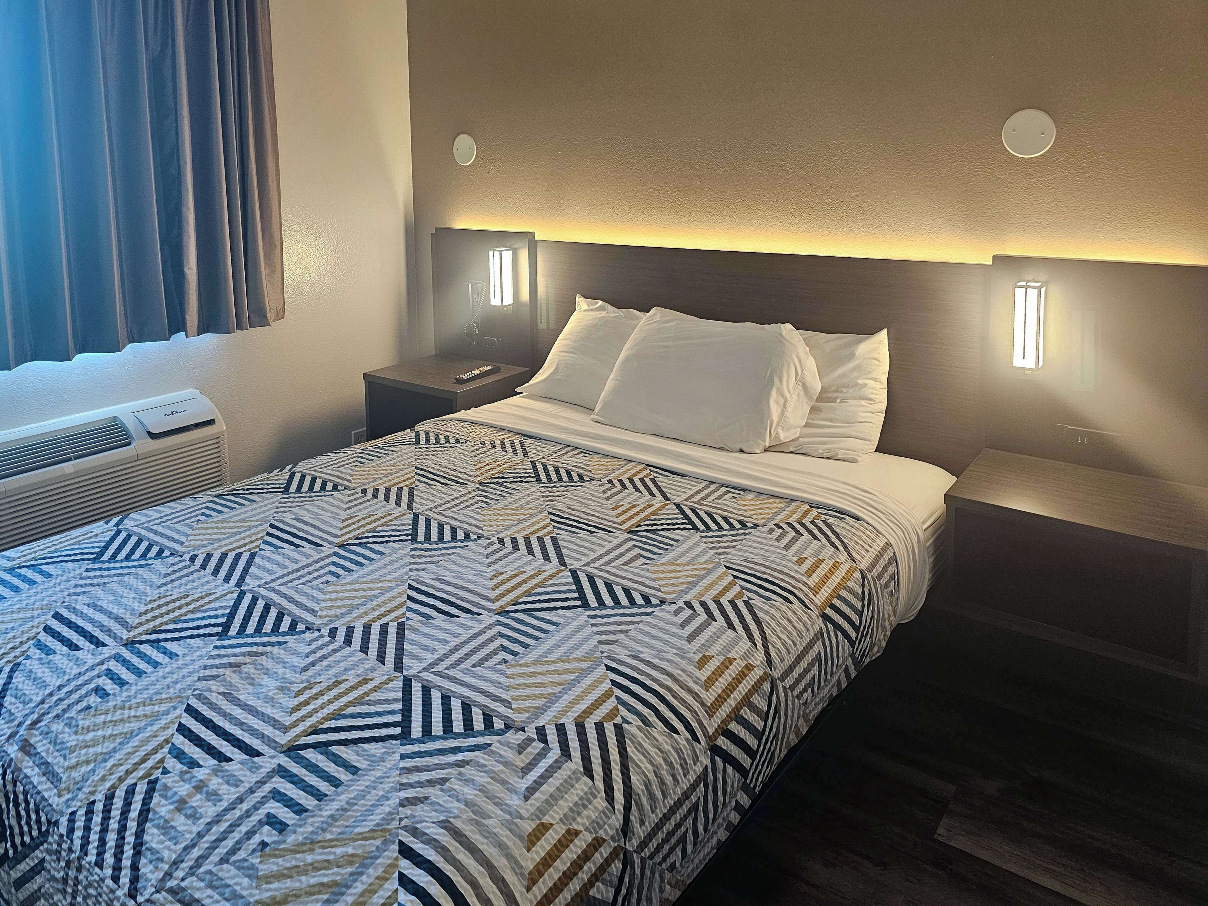 Ein Hotelzimmer mit Bett, Nachttischen, einem Heizgerät und einem Fenster mit Vorhängen.