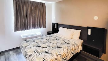 A modern hotel room with a large bed, a bedside table, a wall-mounted TV, and a window with curtains.