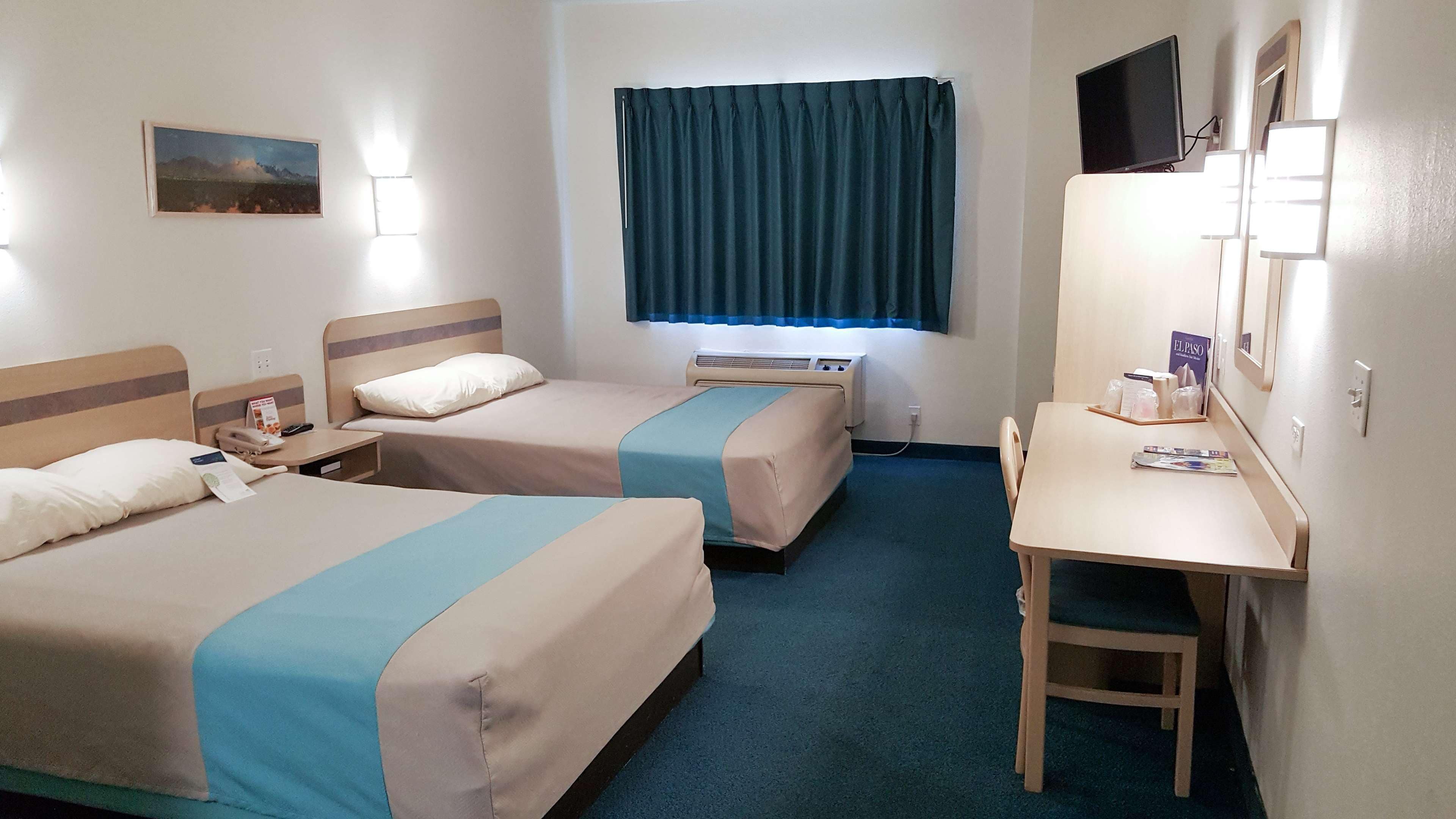 A hotel room with two beds, a desk, a chair, a TV, and a window with curtains.