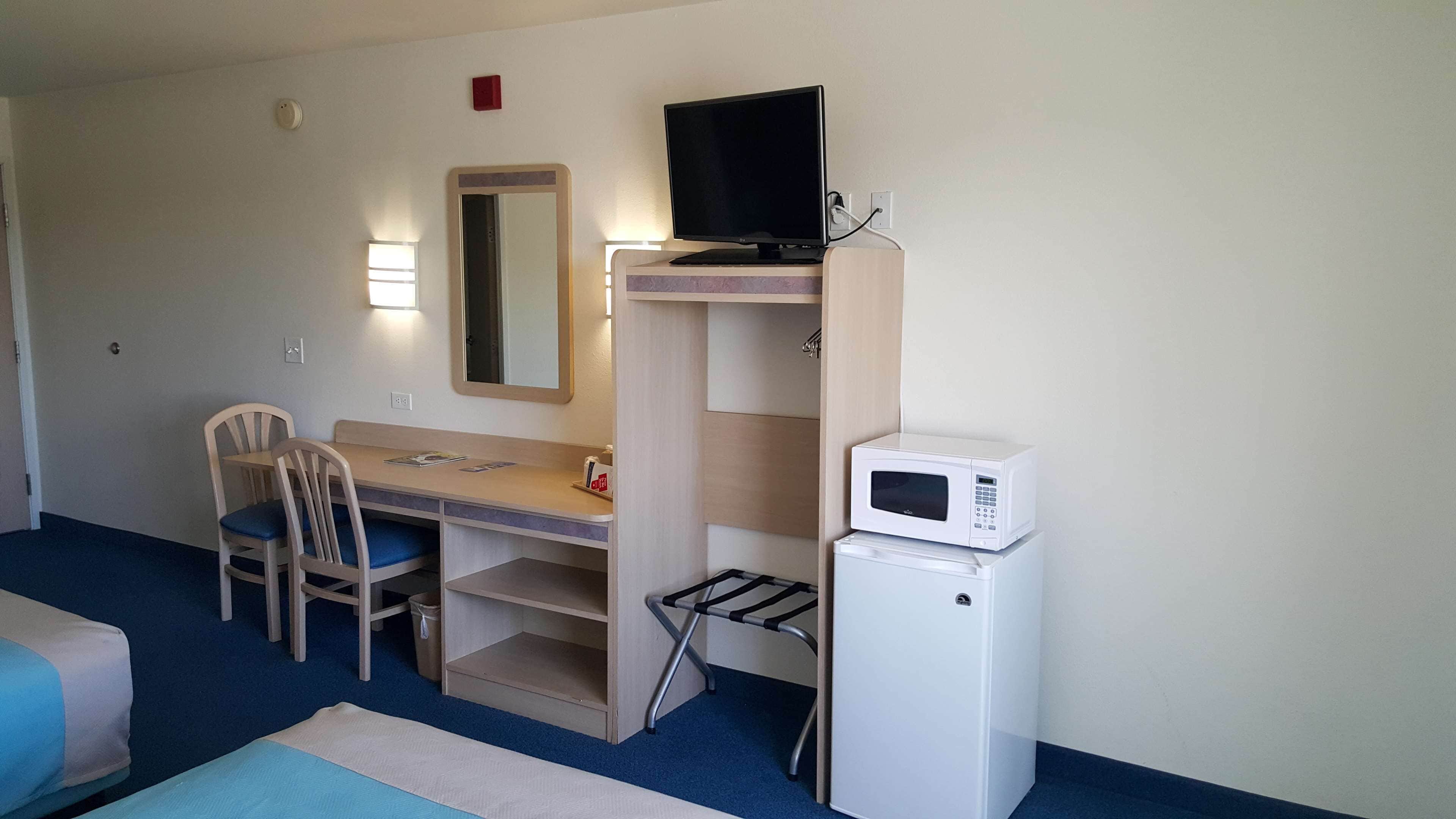 A compact hotel room with a desk, chair, television, and a microwave.
