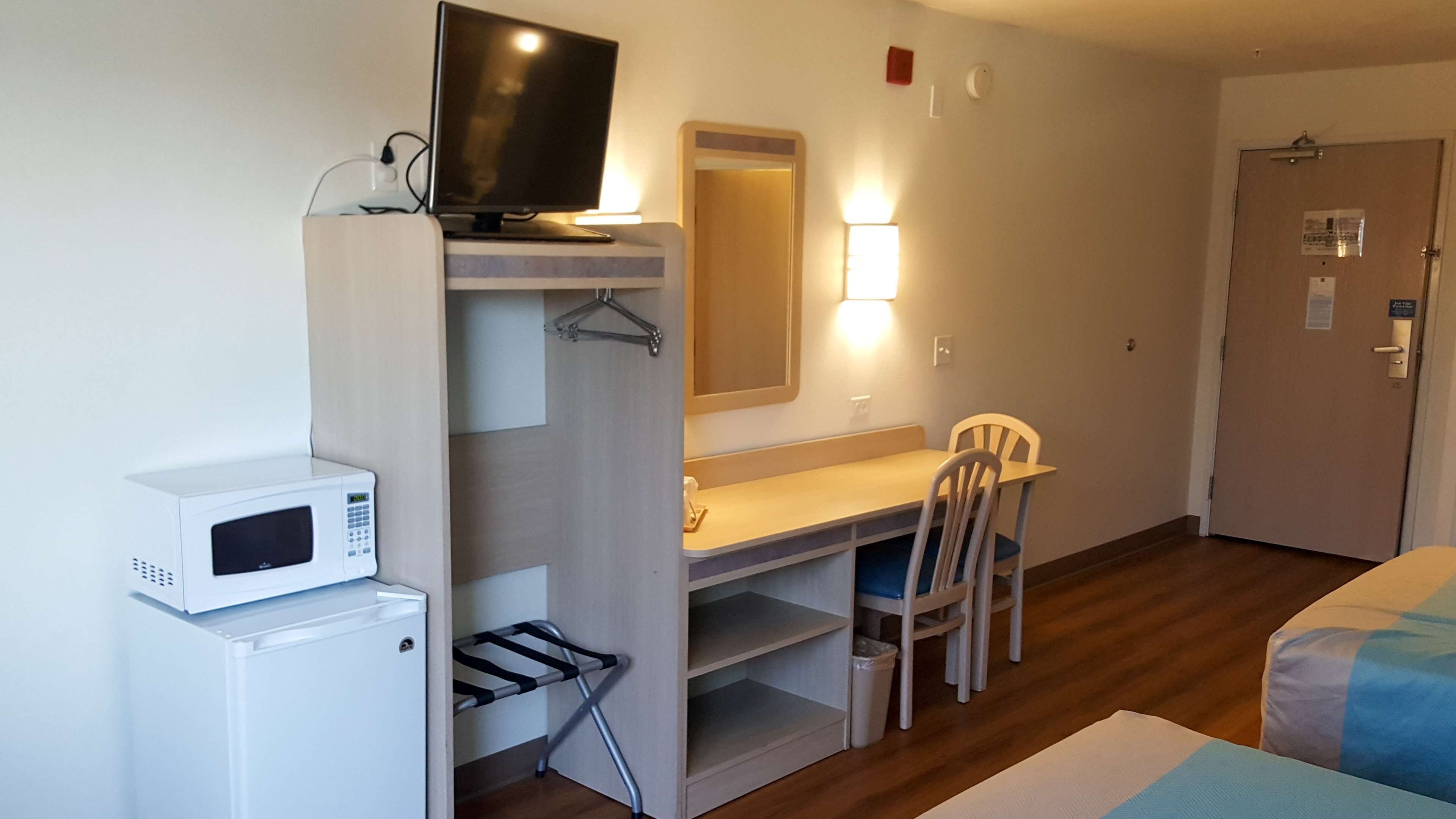 A compact hotel room with a kitchenette, a television, a desk with a chair, and a bed.