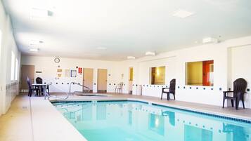 A swimming pool with chairs and a lifeguard chair, a clock, and informational posters on the walls.