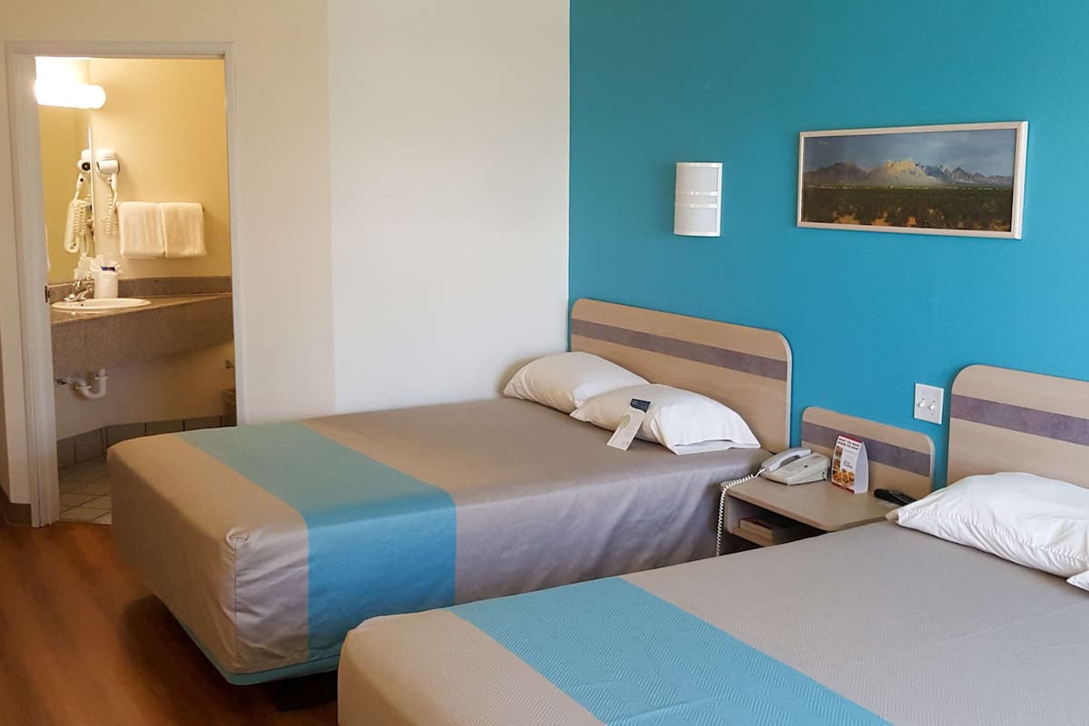 A hotel room with two beds, a bathroom with a sink, and a painting on the wall.