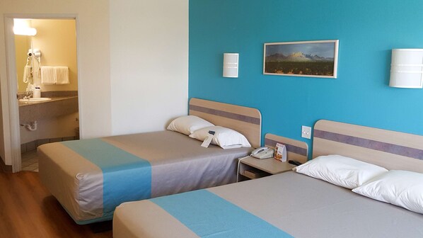 A hotel room with two beds, a bathroom with a sink, and a painting on the wall.