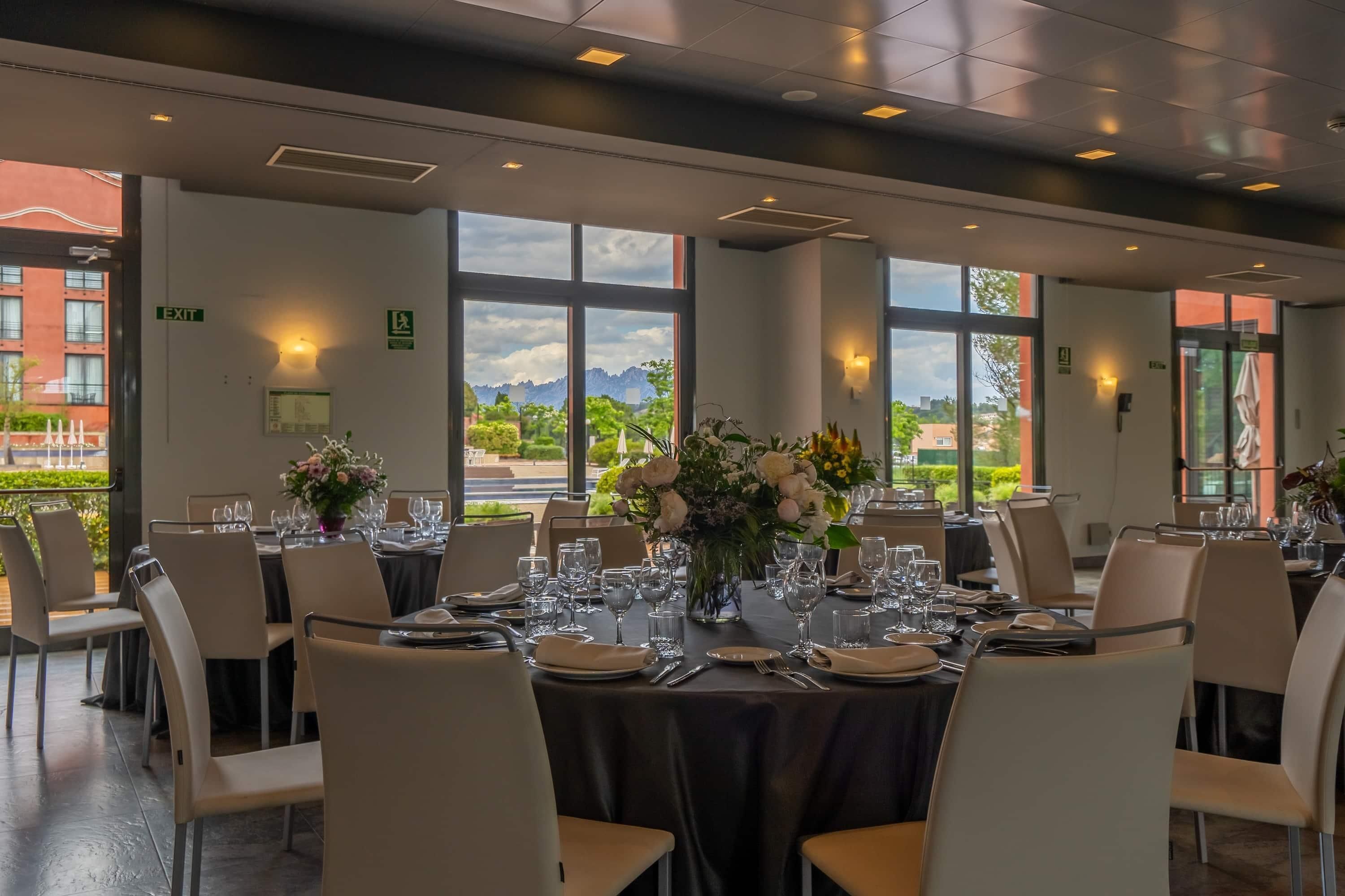 Un restaurante con mesas dispuestas para comer, amplias ventanas con vistas y señales de salida.