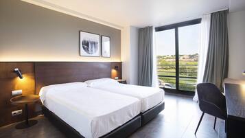 A hotel room with a double bed, bedside tables, a desk, and a large window with curtains.