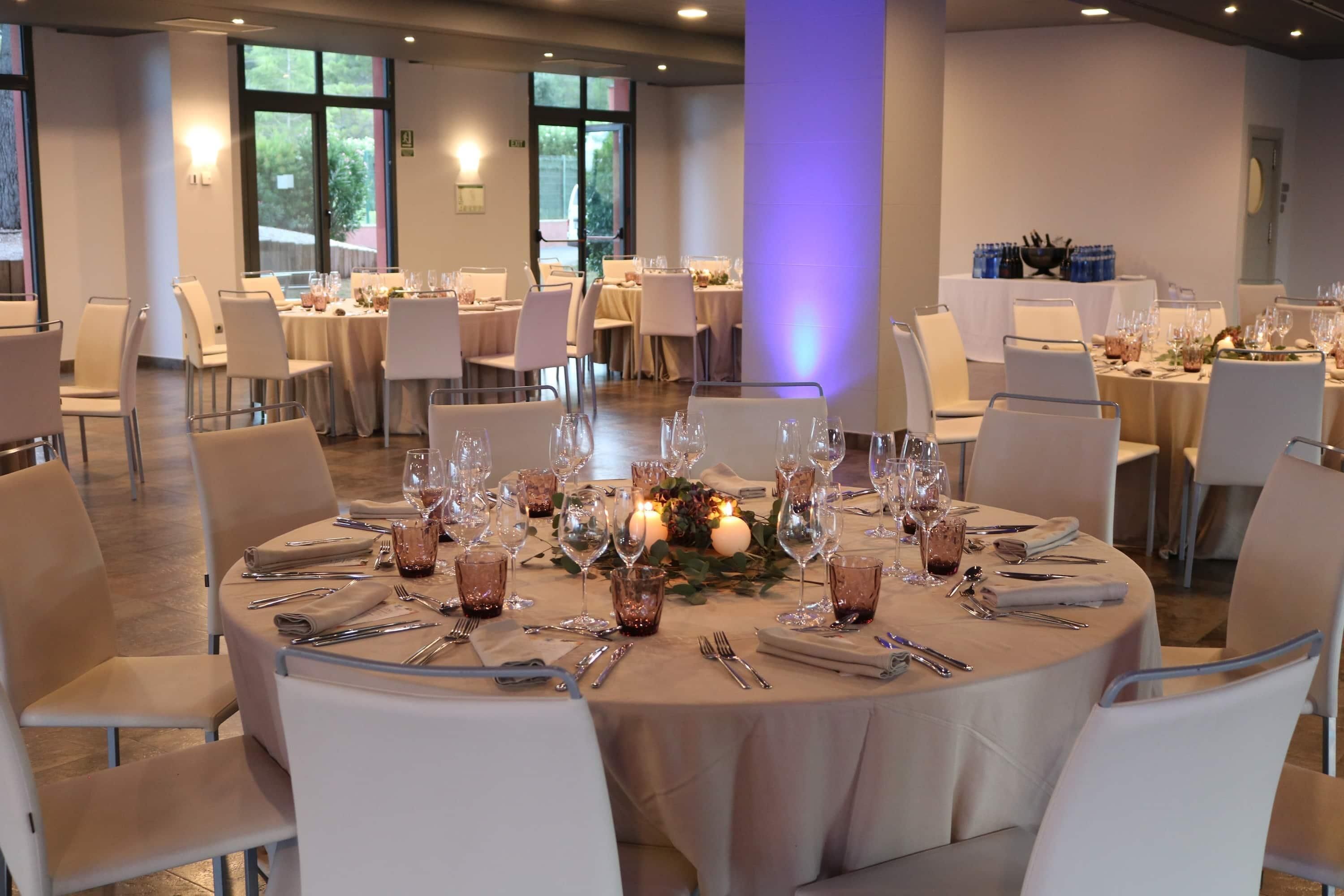 A banquet hall with round tables, chairs, and dining ware.