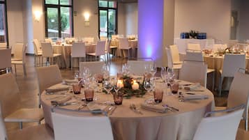 A banquet hall with round tables, chairs, and dining ware.