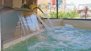 A hot tub with water cascading from a metal structure, surrounded by indoor plants and a view of buildings through large windows. - Dolce by Wyndham Barcelona Resort (Sant Esteve Sesrovires)