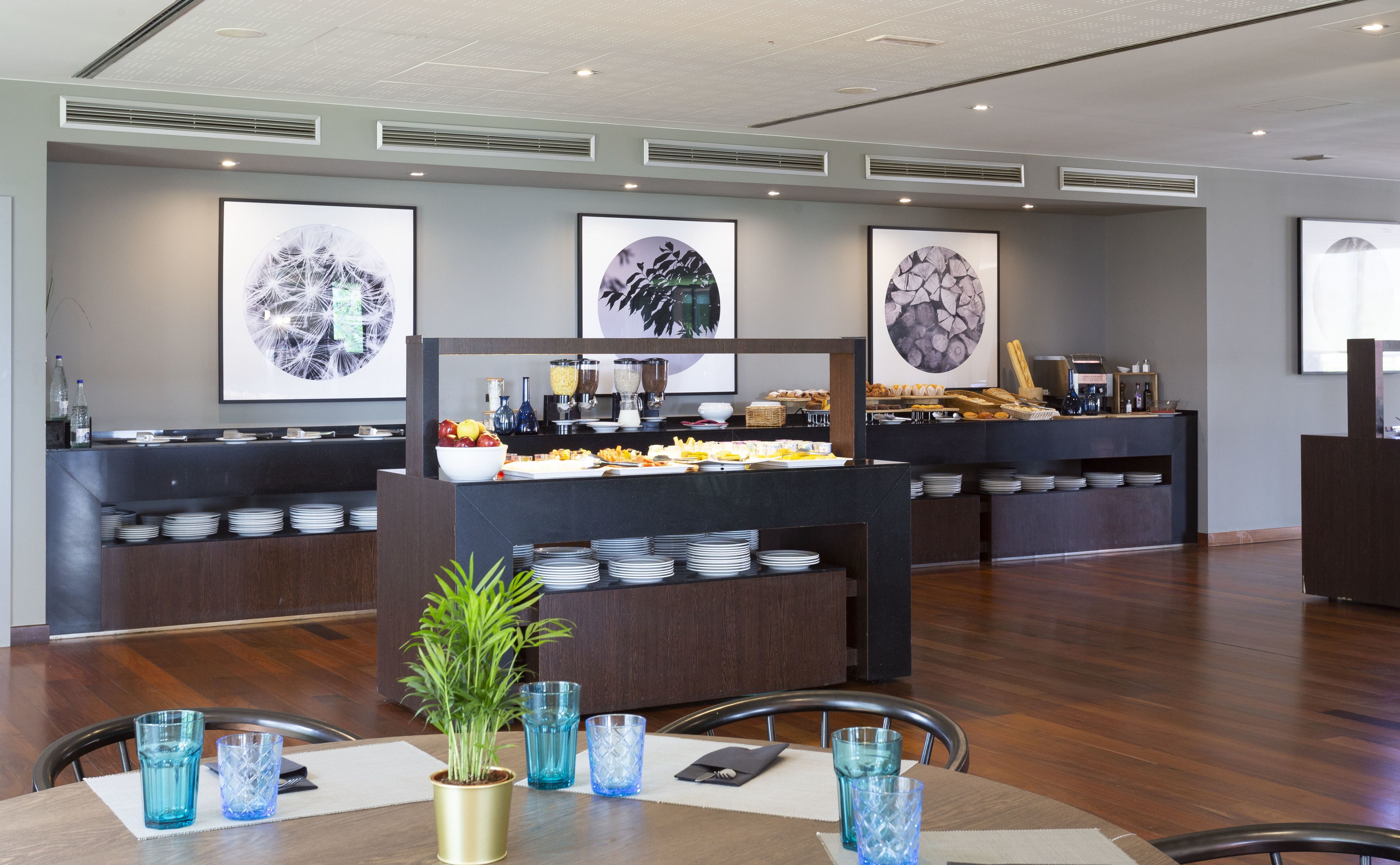 Un área de desayuno de hotel moderna con un sistema de bufé, que incluye diferentes alimentos y bebidas, y obras de arte en las paredes.