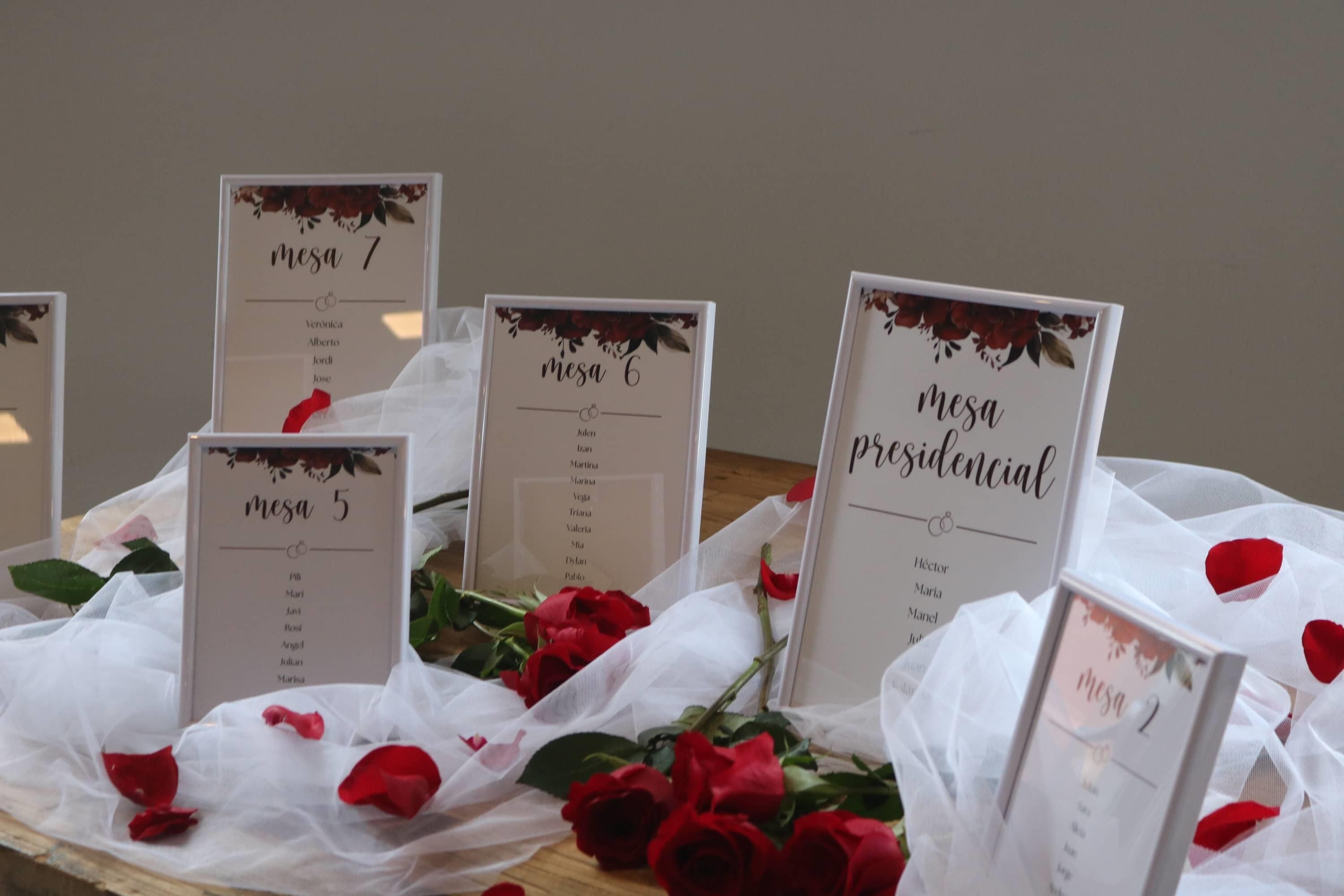 A table with multiple nameplates labeled 'mesa 1' through 'mesa 7,' surrounded by red roses and white fabric.