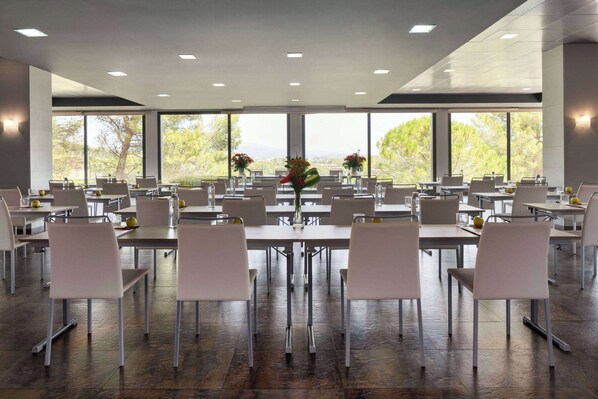 Un comedor espacioso con varias mesas y sillas, ventanas amplias con vistas a árboles y montañas, y un diseño de techo moderno.