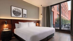 A modern hotel room with a large bed, two wall-mounted lamps, and a view of the outside balcony. - Dolce by Wyndham Barcelona Resort (Sant Esteve Sesrovires)