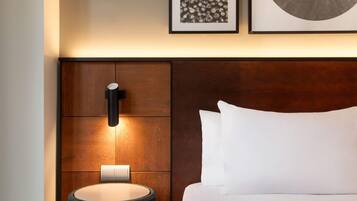 Una habitación de hotel moderna con cabecera de madera, una lámpara de noche y obras de arte enmarcadas en la pared.