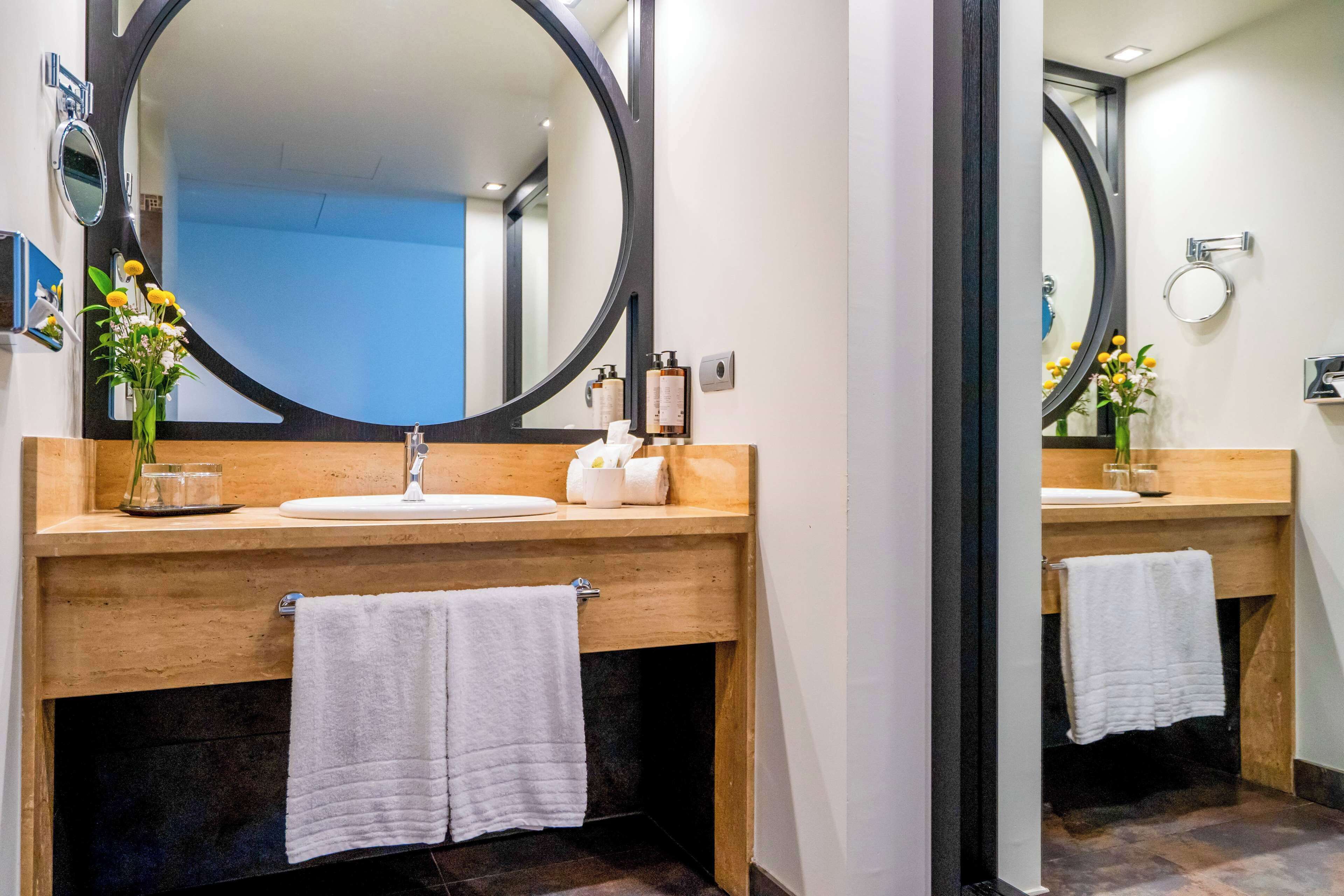 Un baño moderno con tocador de madera, un espejo redondo grande y un lavabo blanco.