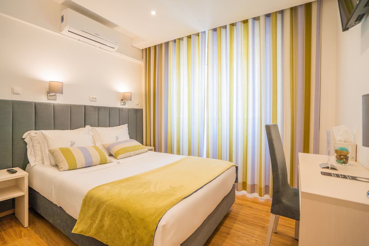 Ein Hotelzimmer mit Bett, Nachttisch, Schreibtisch, Stuhl und einem gestreiften Vorhang.