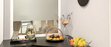 A hotel reception desk with a clock, a fruit bowl, a glass pitcher, and a tray of pastries.
