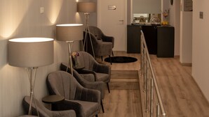 Een hotel lobby met een receptiebalie, een zithoek met fauteuils en vloerlampen, en een houten vloer.