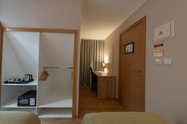 Una habitación de hotel con cama, escritorio con lámpara, armario y zona de ducha.