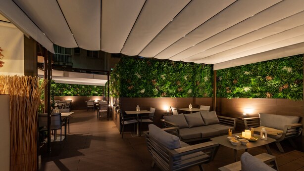 Een terras met tafels en stoelen, een groene wand met planten en een houten plafond.
