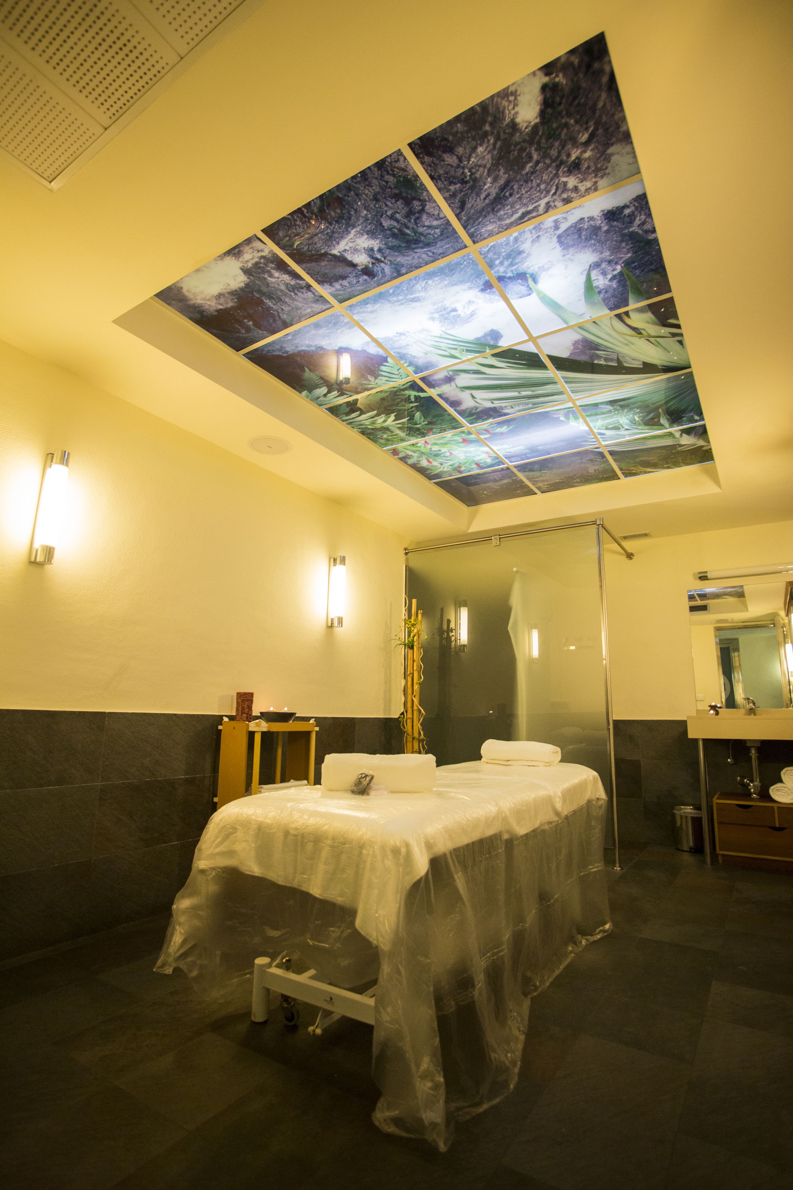 A hotel bathroom with a large skylight, a bed with a white cover, a mirror, and a sink.
