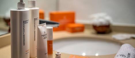 Un tocador de baño con artículos de aseo, incluyendo una botella de leche limpiadora facial Germaine de Capucine, un tubo de crema y un cepillo.