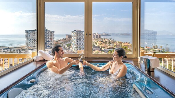 A couple in a hot tub with a cityscape view.