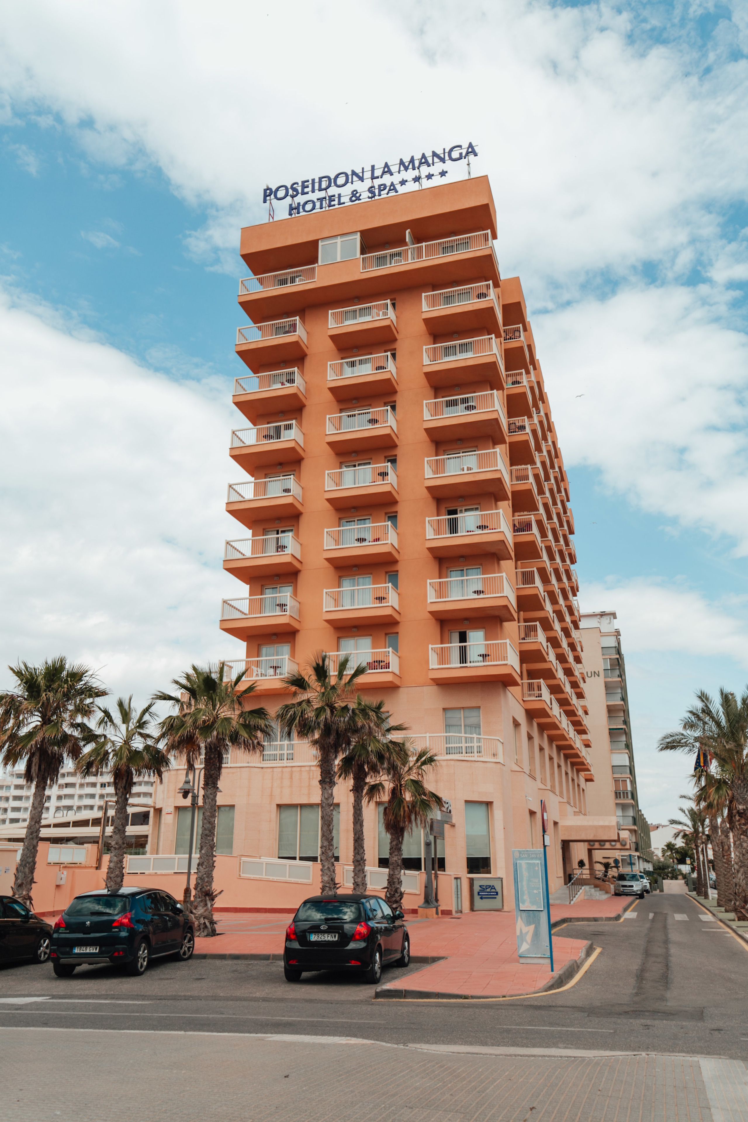 Un hôtel à plusieurs étages, appelé Poseidon La Manga, doté de balcons, de palmiers et offrant une vue sur un ciel dégagé.