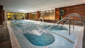 A large indoor hot tub area with multiple seating areas and a stone wall backdrop.