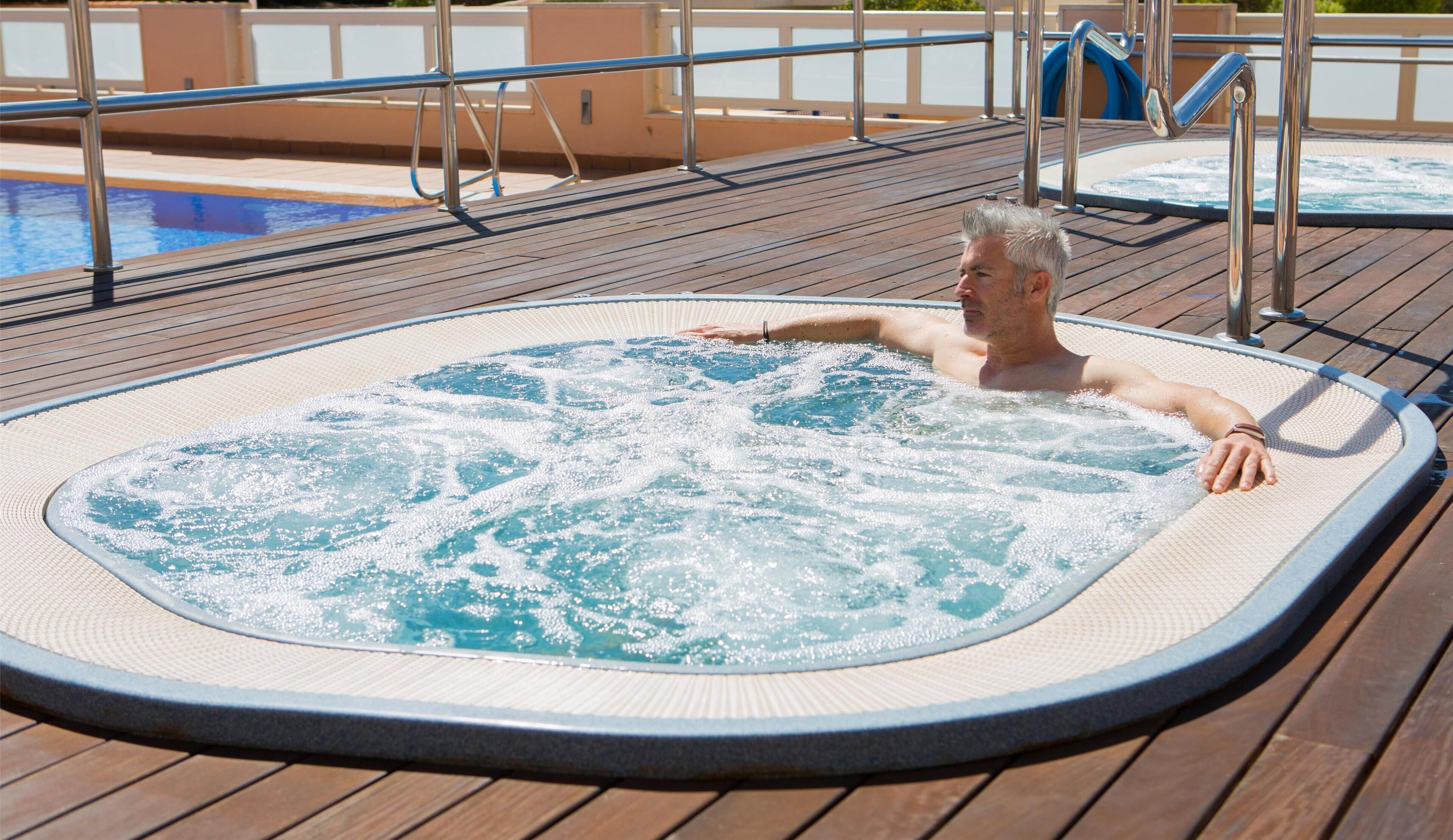 Un jacuzzi en una terraza de madera con una piscina al fondo.