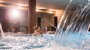 A couple relaxing in a hot tub with a waterfall feature.