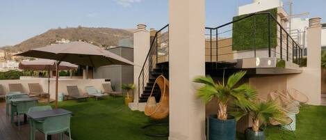 Terraza en la azotea con mobiliario exterior, una silla colgante y una escalera que sube a un nivel superior.