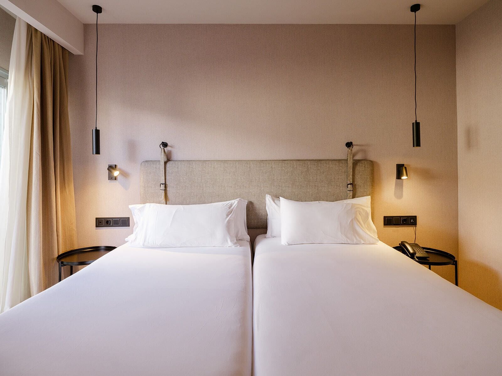 Una habitación de hotel con dos camas, mesitas de noche, un teléfono y lámparas fijadas a la pared.