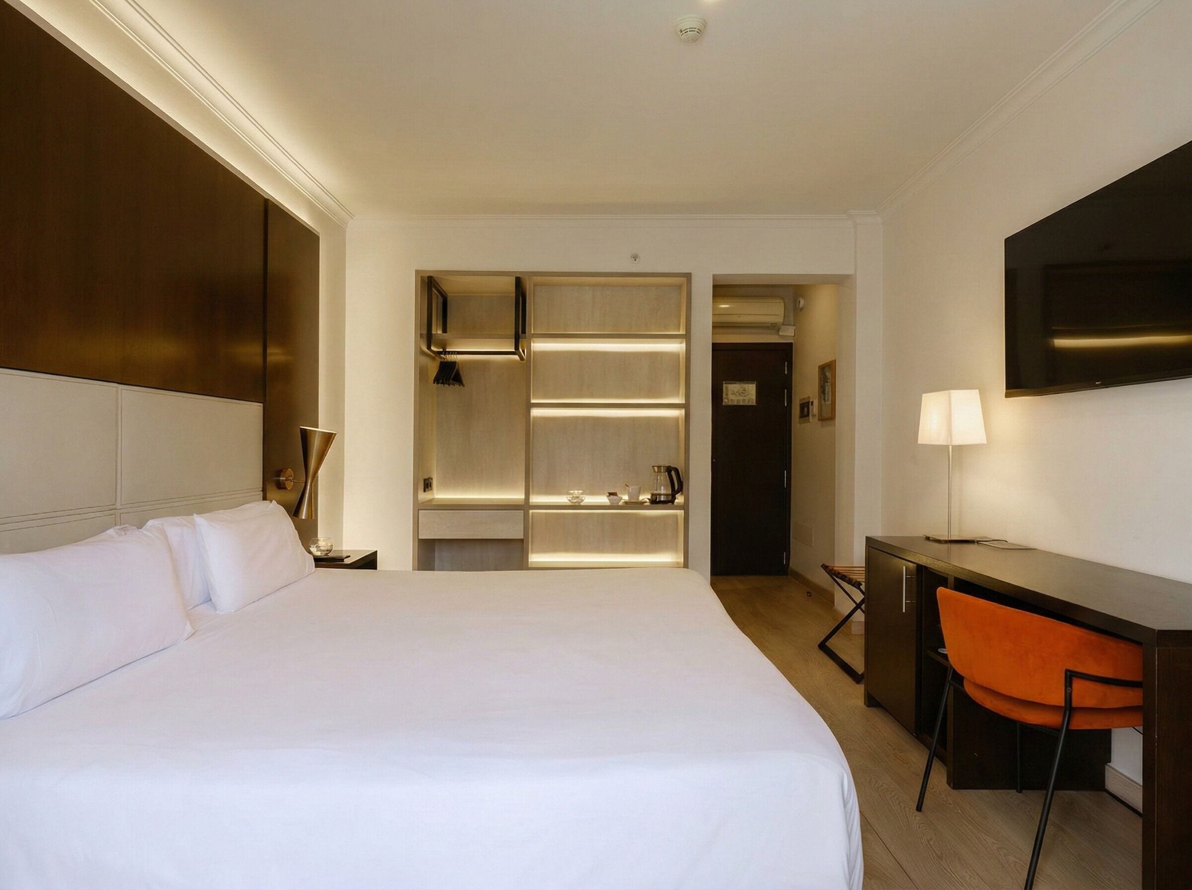 Ein Hotelzimmer mit einem großen Bett, einem Schreibtisch mit Stuhl, einem Fernseher und einem begehbaren Kleiderschrank mit Regalen.