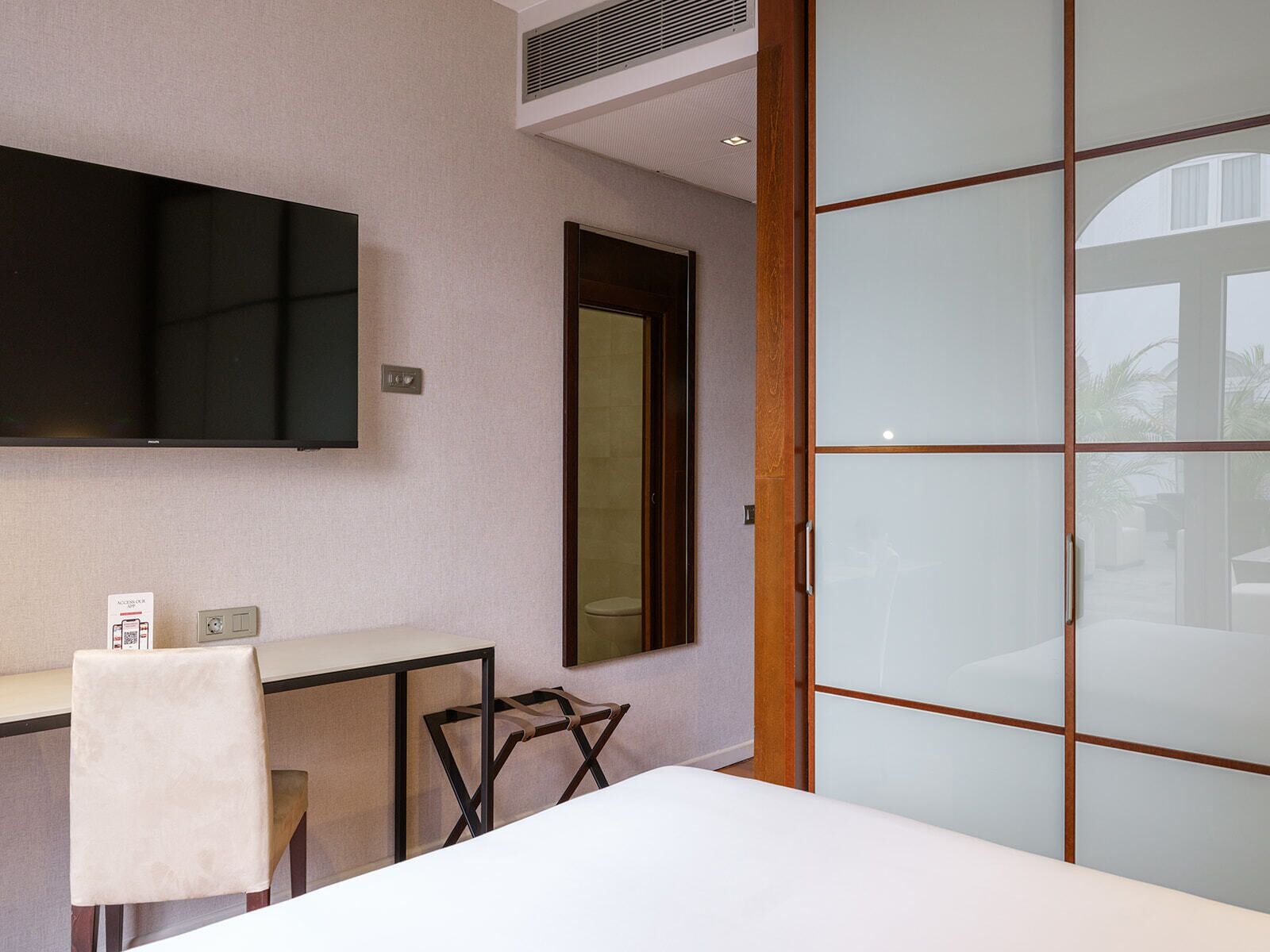 A modern room with a bed, a desk, a chair, a TV, and a sliding door.