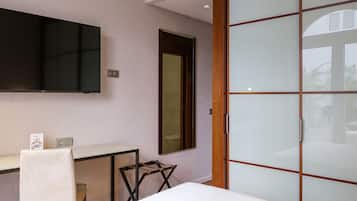 A modern room with a bed, a desk, a chair, a TV, and a sliding door.