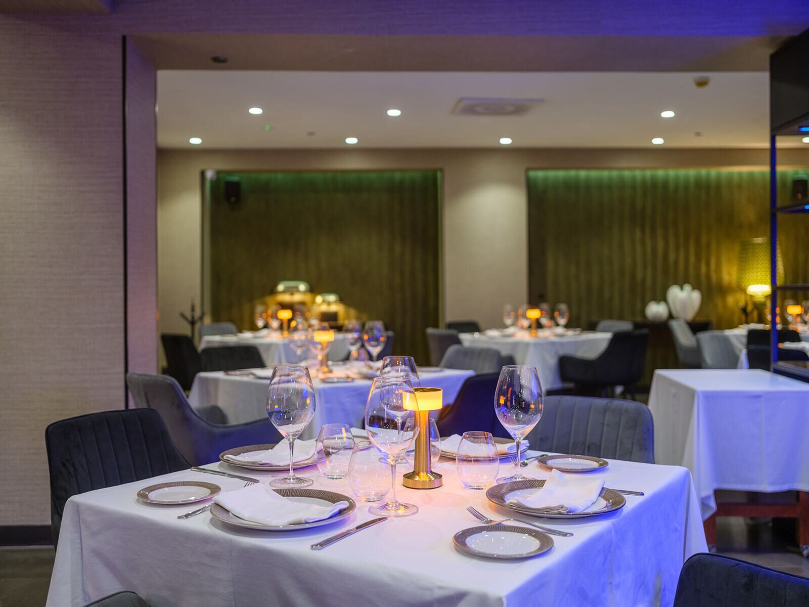 A restaurant with tables set for dining, featuring white tablecloths, plates, and wine glasses.
