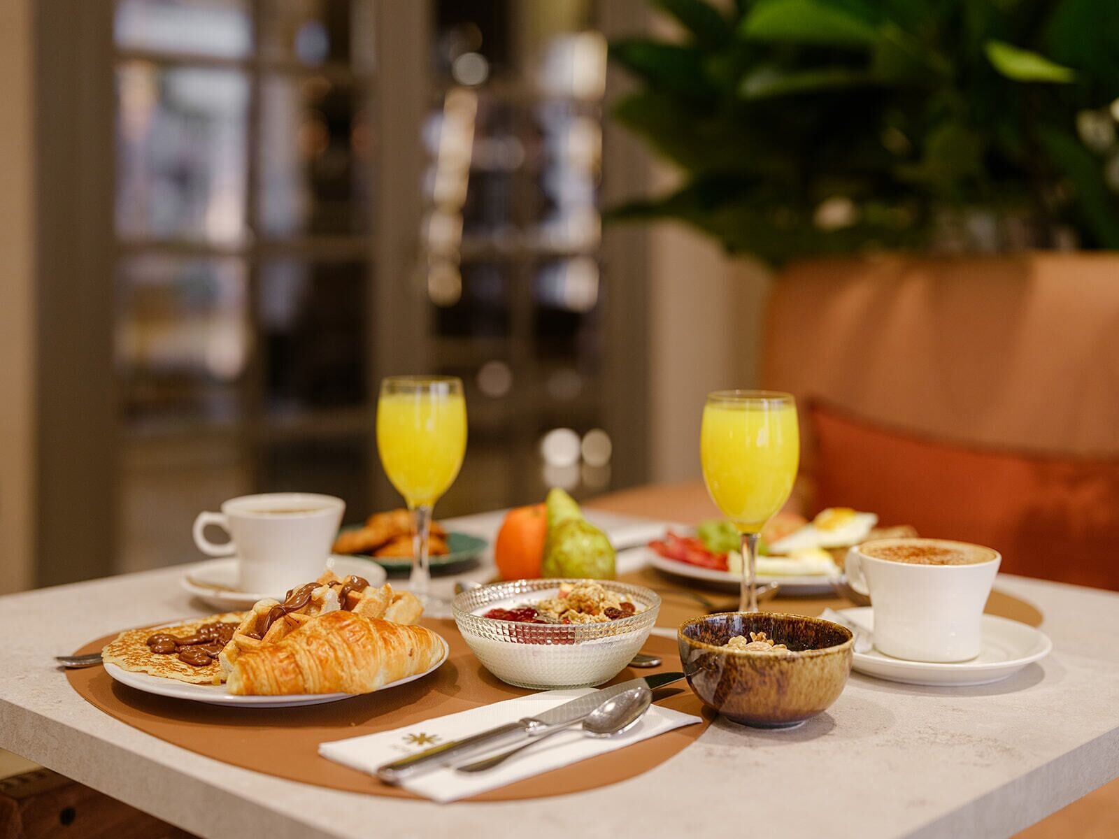 A breakfast setting with croissants, cereal, and orange juice on a table.