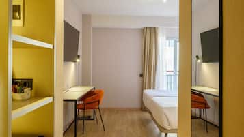 Ett hotellrum med en säng, två skrivbord, en spegel och ett fönster med gardiner.