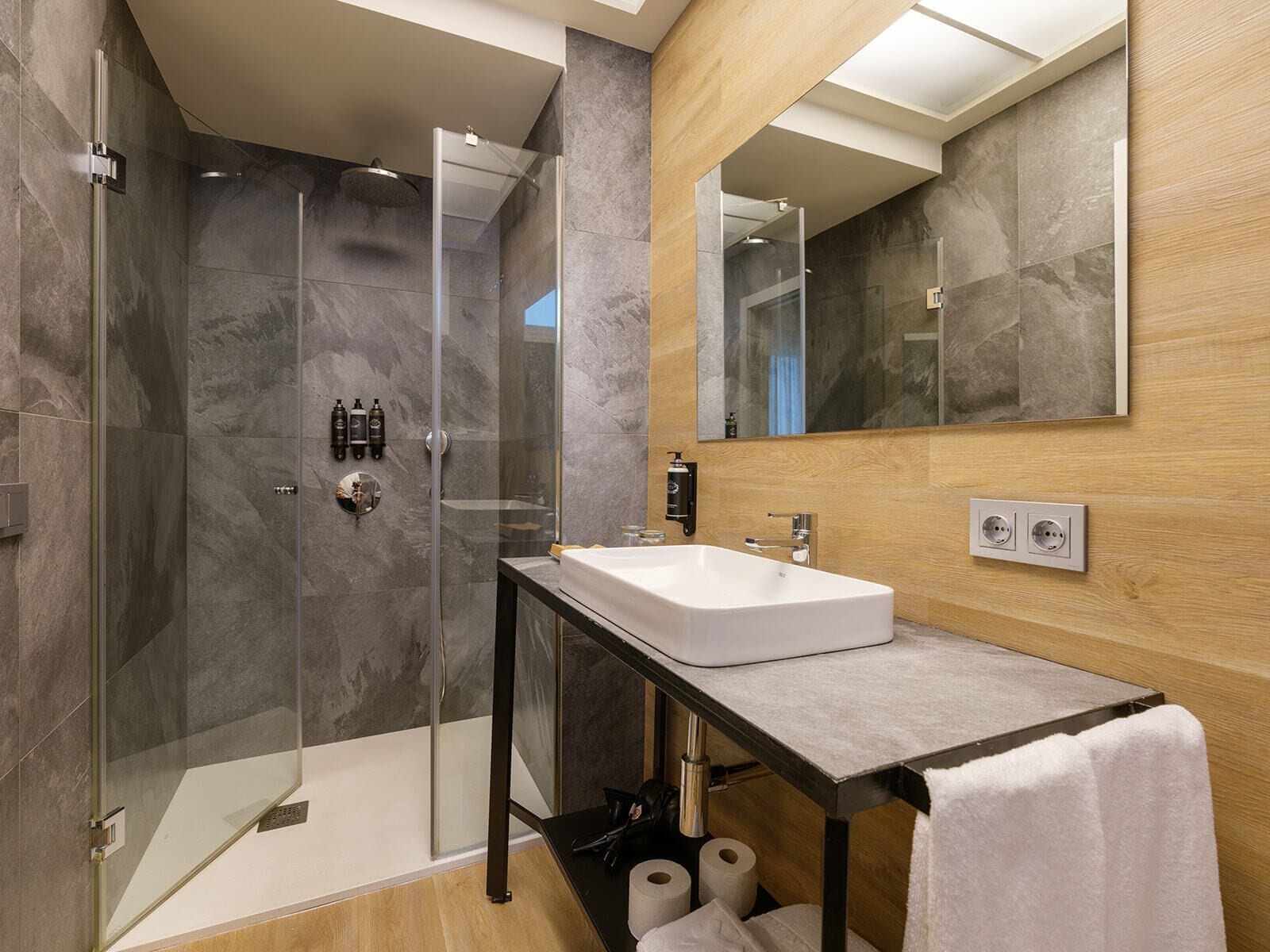 Un baño moderno con ducha de vidrio, lavamanos blanco y tocador de madera.