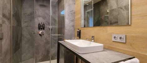 Un baño moderno con ducha de vidrio, lavamanos blanco y tocador de madera.