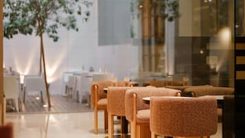 Interior moderno de restaurante com área de estar, mesas e cadeiras de madeira, divisória de vidro e uma janela grande.