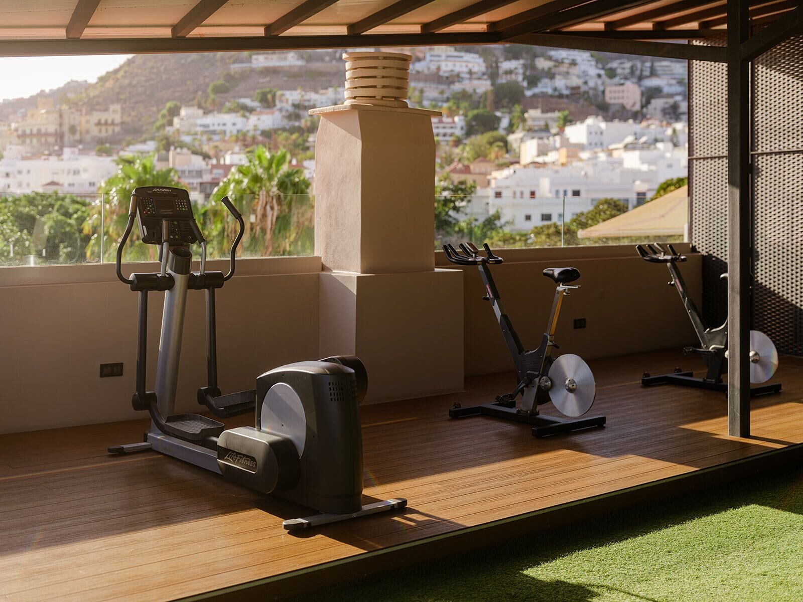 A rooftop gym with stationary bikes and a rowing machine, overlooking a cityscape.