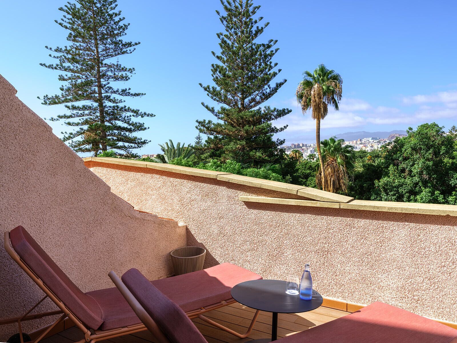 A rooftop terrace with two lounge chairs, a small table, and a water bottle.