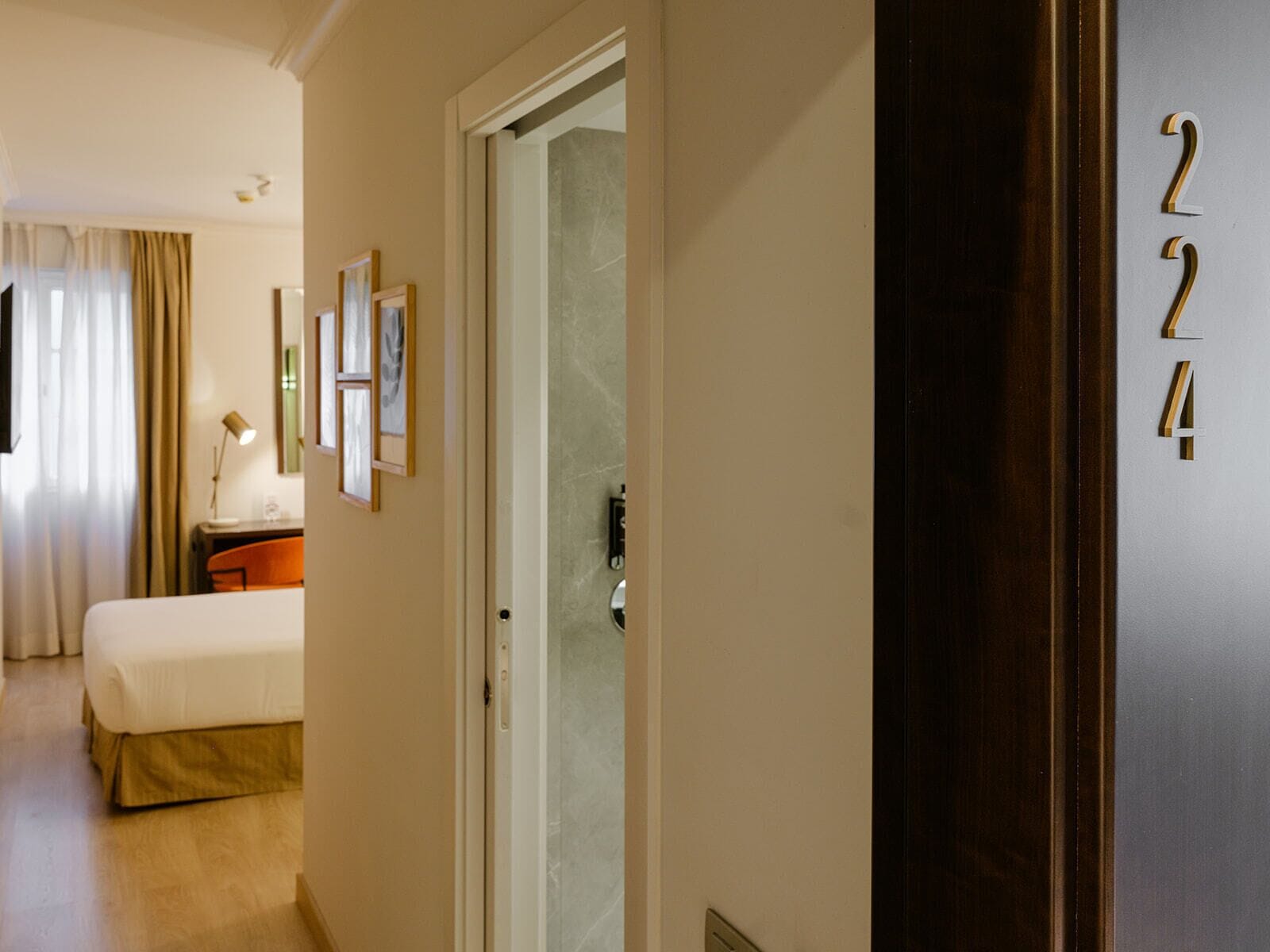 Habitación de hotel con cama, escritorio, silla, lámpara y puerta con el número 224.