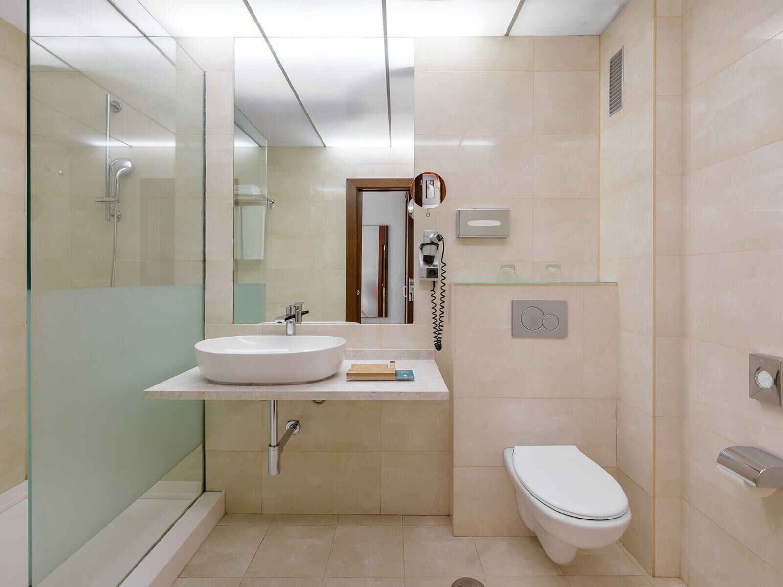 Un baño moderno con cabina de ducha de vidrio, un lavamanos blanco, un inodoro y un espejo.