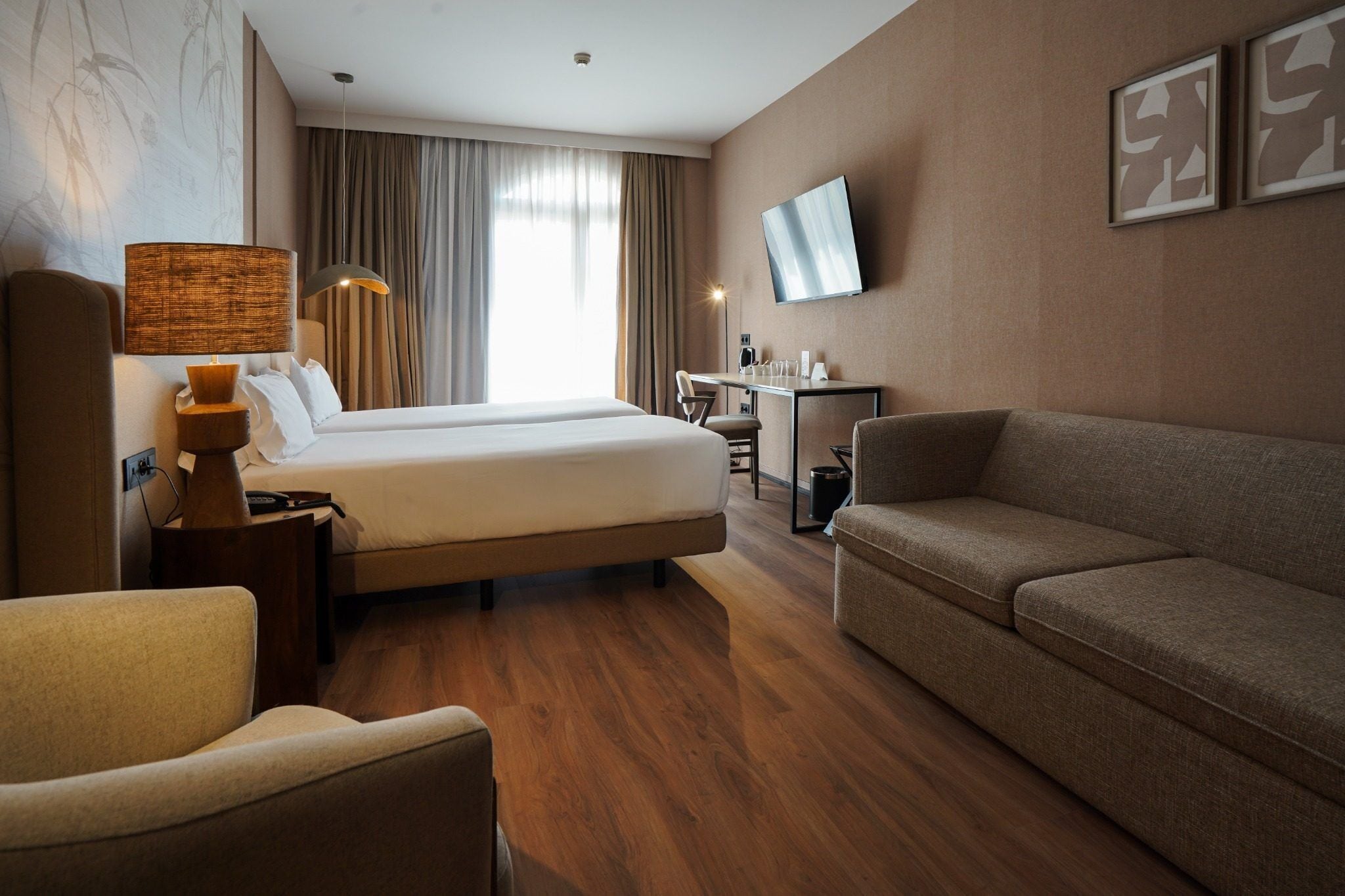 A hotel room with a bed, a sofa, a desk, a lamp, and a TV.