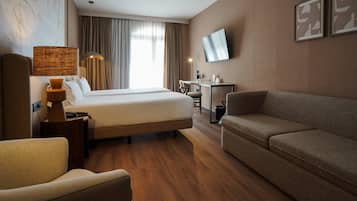 A hotel room with a bed, a sofa, a desk, a lamp, and a TV.