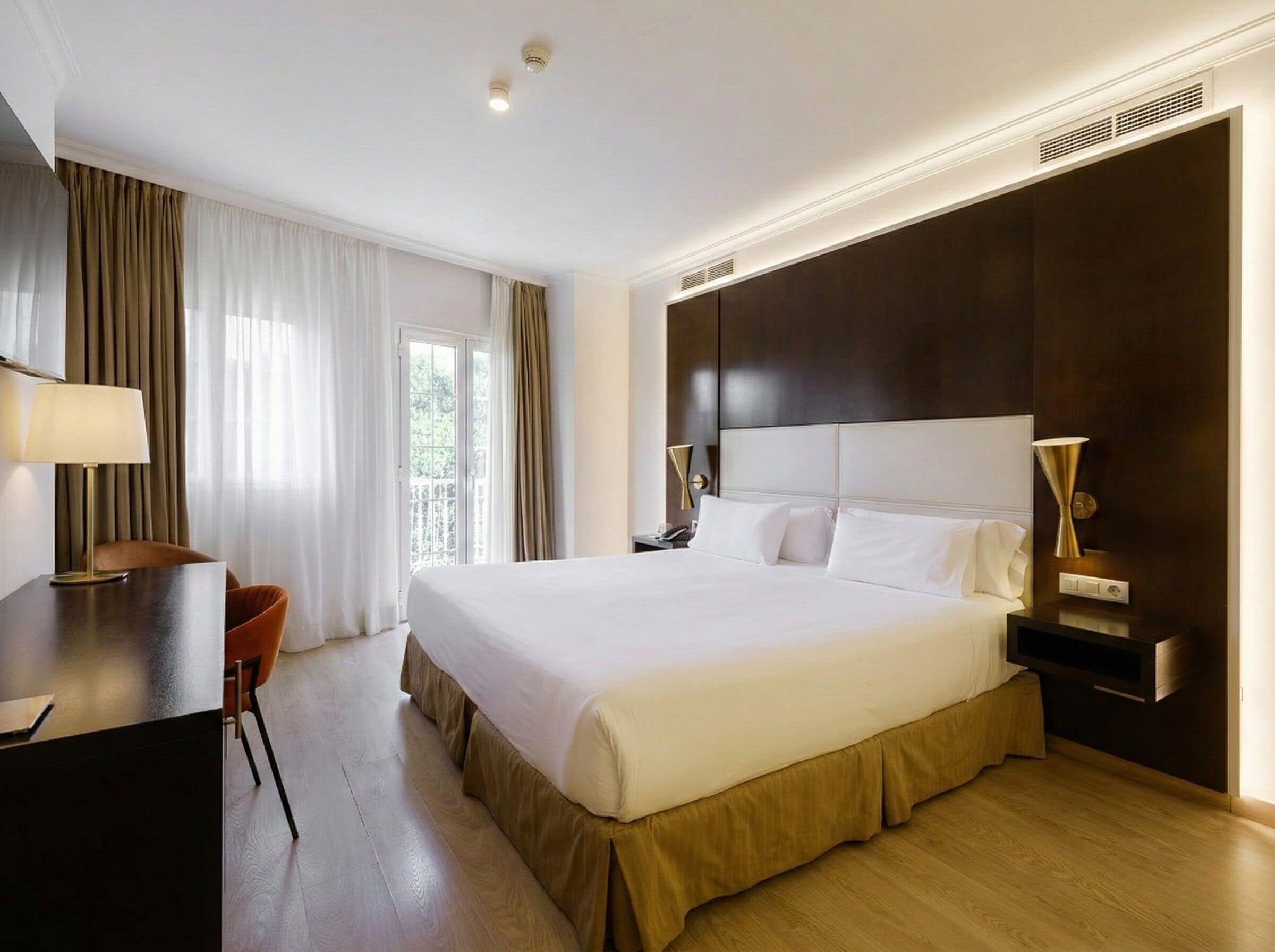 Una habitación de hotel con una cama grande, un escritorio, una silla y una mesita de noche.